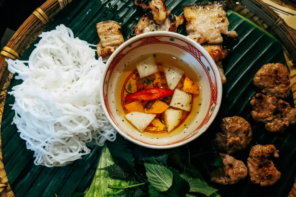 Bun Cha served with grilled pork, noodles, and fresh herbs on banana leaf