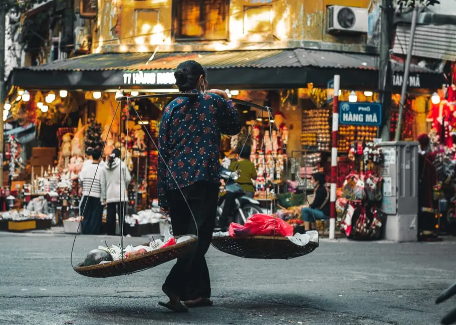 a_local_vendor_carrying_baskets_with_goods_in_a_vibrant_hanoi_street_m.webp