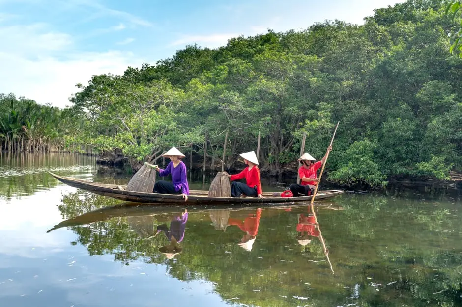 fishermen navigate a river in a wooden boat surrounded by lush mangroves